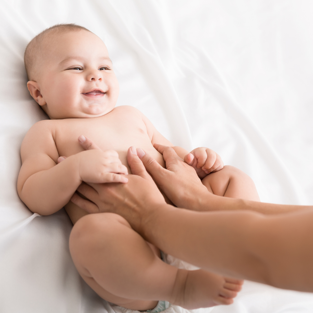 Smiling baby lying on a soft white blanket receiving a gentle infant massage
