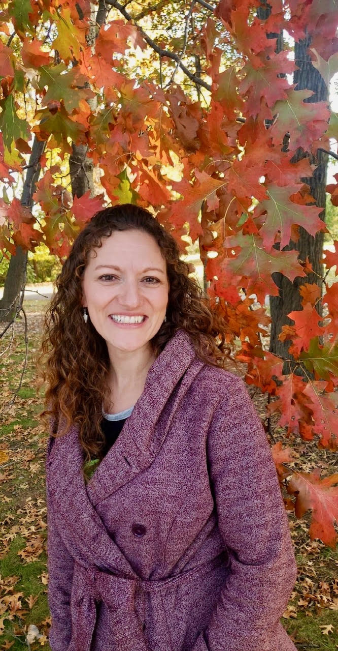 Natasha Galloway, licensed massage therapist, smiling outdoors among autumn leaves